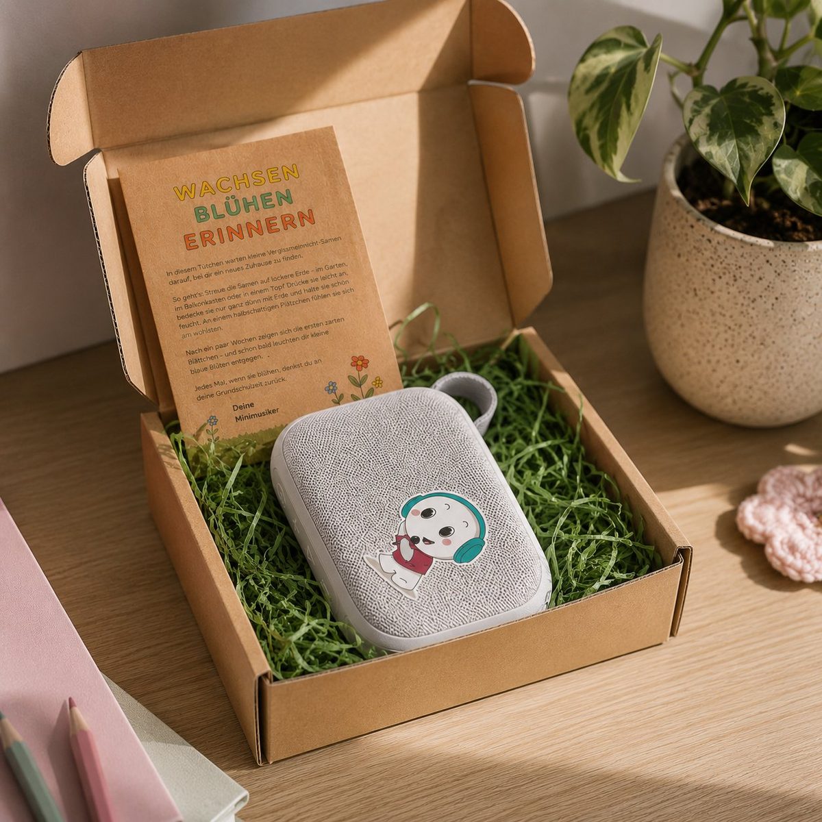 Geöffneter Versandkarton mit der Bluetooth-Box auf grünem Füllmaterial und Samentütchen daneben.
